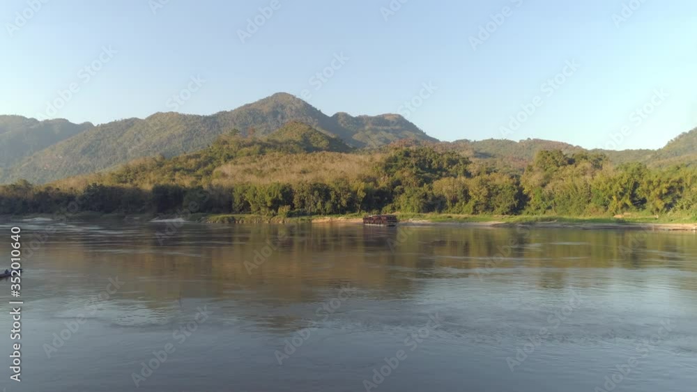 Aerial shot of boats in river against sky on sunny day, drone flying forward towards green mountains - Mekong River, Laos Aerial shot of boats in river against sky on sunny day, drone flying forward towards green mountains - Mekong River, Laos