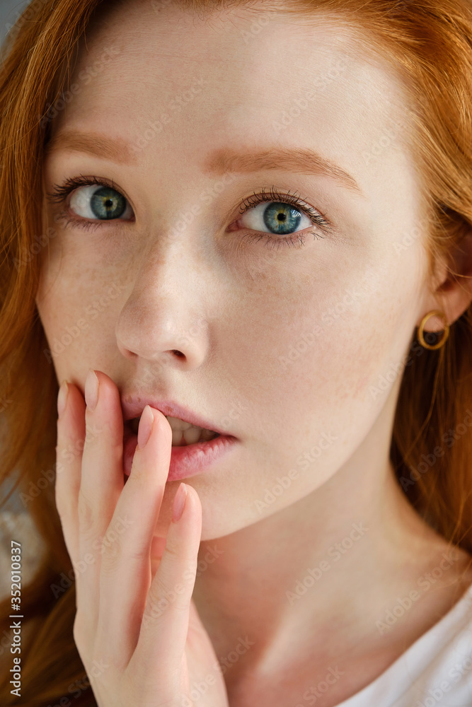 A close portrait of a beautiful red-haired girl with blue eyes. Looks into the frame and pressing his fingers to his lips A close portrait of a beautiful red-haired girl with blue eyes. Looks into the frame and pressing his fingers to his lips