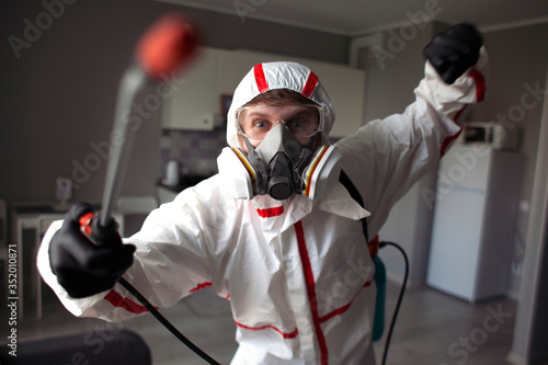 pest control. A worker in a protective suit disinfects the room with a chemical agent, a person in a respirator sprays in the apartment