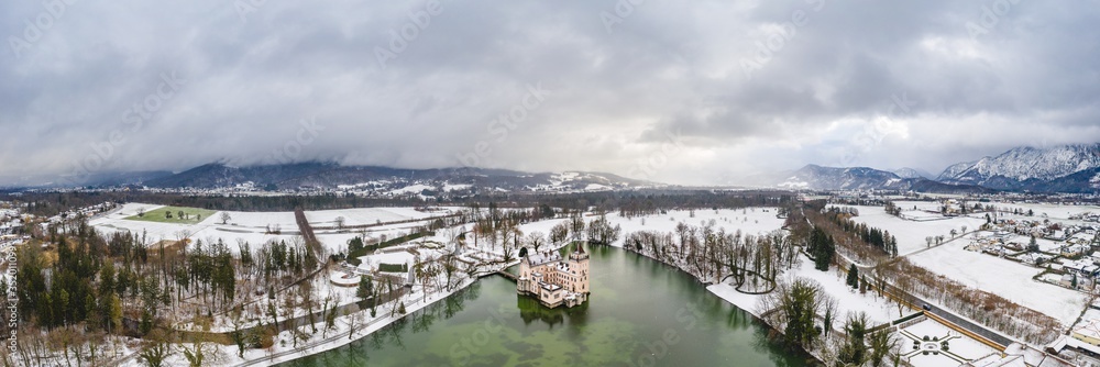 Panoramic aerial view of Schloss Anif castle moated in artificial pond at Salzburg outskirts in heavy snow during winter view of untersberg mountain