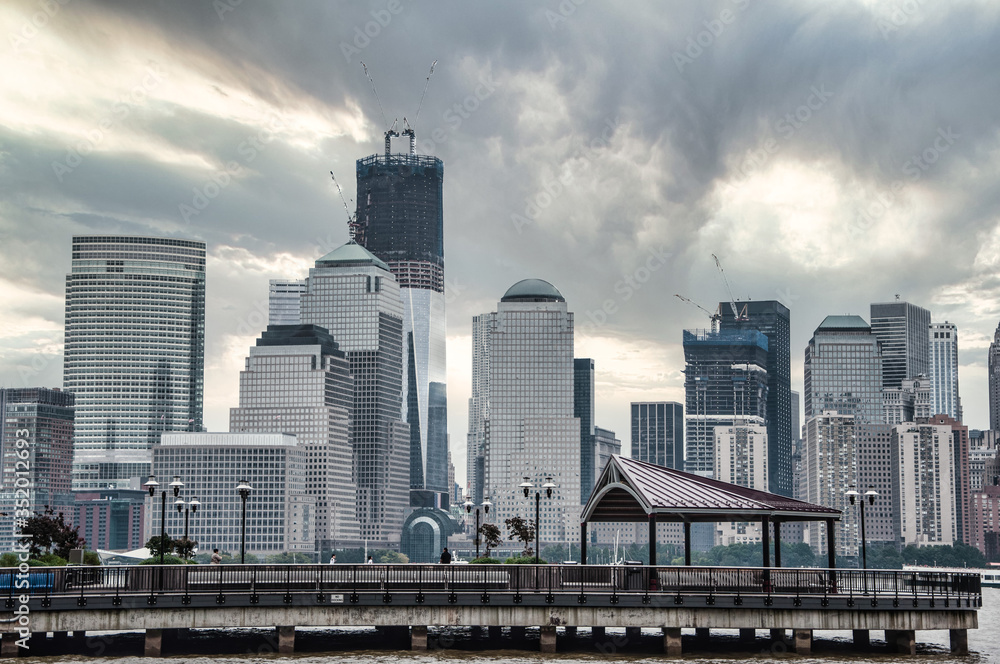 New York City skyline with reconstruction of tower, built up to 80th floor, against a dark, cloudy sky, across the Hudson with a dock in the foreground. New York City skyline with reconstruction of tower, built up to 80th floor, against a dark, cloudy sky, across the Hudson with a dock in the foreground.