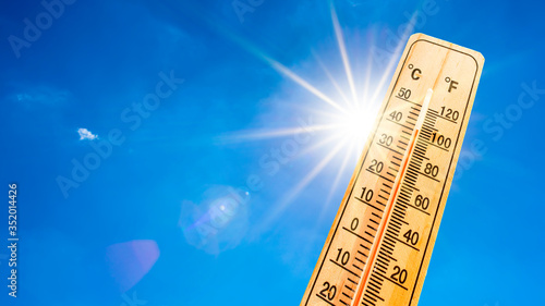 Summer background - blue sky with bright sun and thermometer photo