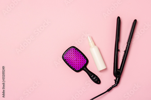 Hair straightener, comb and hair care product on a pink background. Concept of hair care, hairstyle, beauty salon, hairdresser. Flat lay, top view