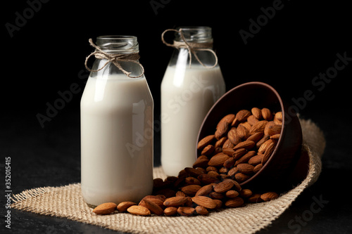 almond milk in glass bottles on a dark background with nuts, vegetarian milk without sugar and lactose