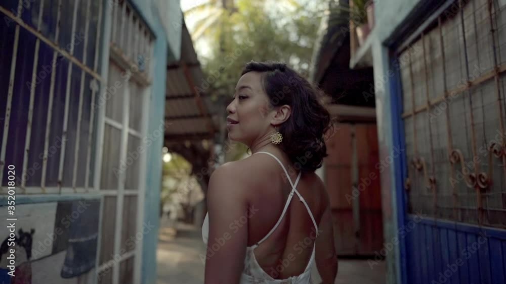 Beautiful woman on vacation walks through narrow street discovering her surroundings turning with alluring look inviting to come along Beautiful woman on vacation walks through narrow street discovering her surroundings turning with alluring look inviting to come along