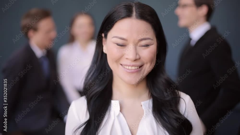 Asian freelancer woman standing in the room with freelancers behind her blurred and showing thumb up sign as everything perfect. Prores 422 Asian freelancer woman standing in the room with freelancers behind her blurred and showing thumb up sign as everything perfect. Prores 422