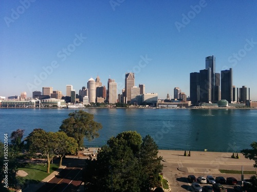Downtown Detroit, Michigan, USA - City skyline with a mixture of modern and historic skyscrapers beneath a blue sky with the Detroit River and a park in the background. This was taken in Windsor, CA.