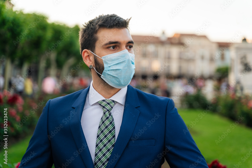 Young attractive business man with mask, blue suit and tie in outdoor park Young attractive business man with mask, blue suit and tie in outdoor park