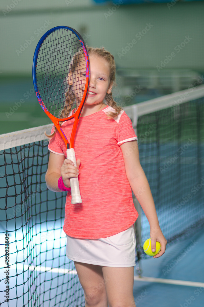 A happy playful girl smiles mischievously on the tennis court with a racket.