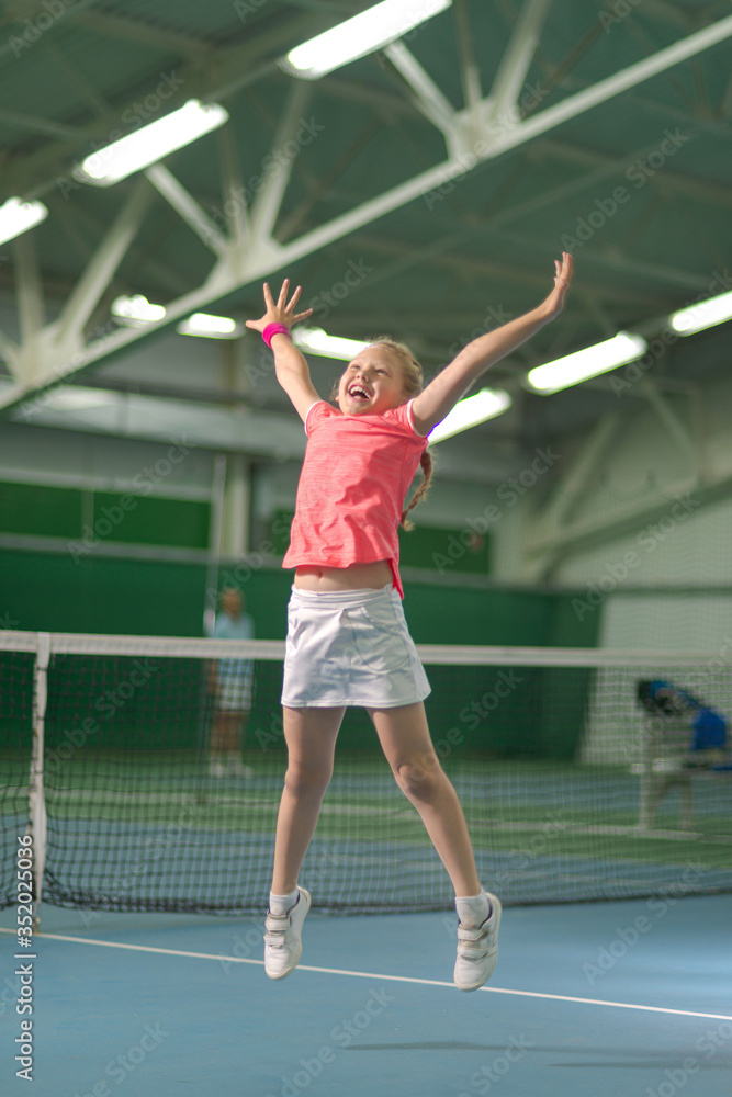 A little girl on an indoor tennis court is happy that she just won a tennis match. A little winner.