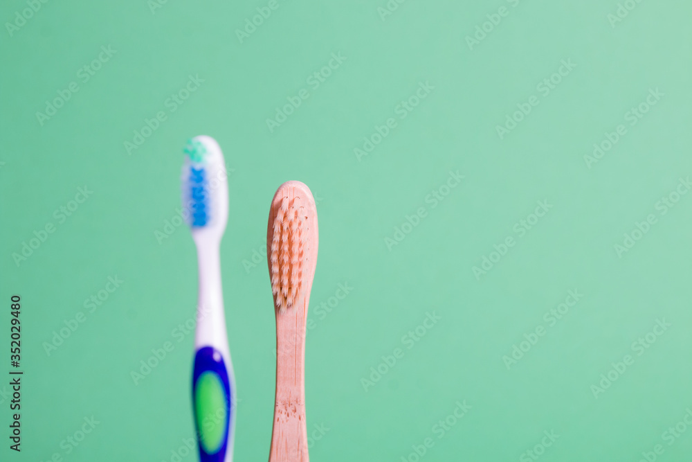 bamboo and plastic toothbrushes on a green background, eco friendly lifestyle concept, plastic pollution of the planet, zero waste and say no to the plastics concept bamboo and plastic toothbrushes on a green background, eco friendly lifestyle concept, plastic pollution of the planet, zero waste and say no to the plastics concept