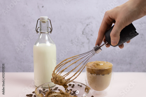 Metal whisk with cream from coffee and sugar. Culinary whisk in woman hand. Cold coffee drink and desert. photo