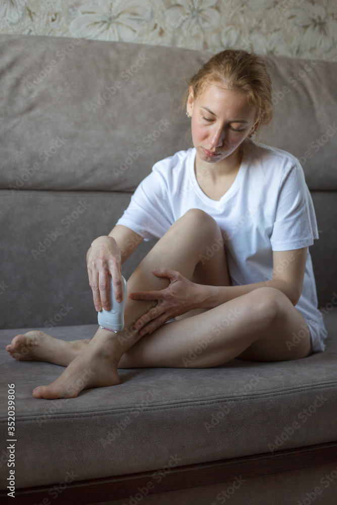 Φωτογραφία Woman does legs depilation with electric epilator at home on the sofa, vertical orientation
