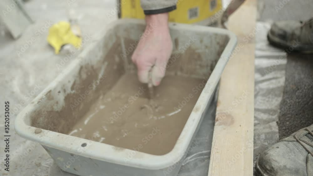 A Man's Hand With Spatula Mixes Liquid Solution In Wheelbarrow For Construction Consisting Of Water, Cement, Gypsum And Sand A Man's Hand With Spatula Mixes Liquid Solution In Wheelbarrow For Construction Consisting Of Water, Cement, Gypsum And Sand
