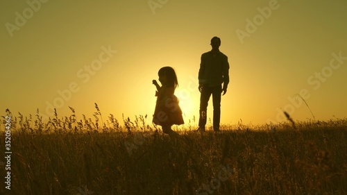 Happy healthy child with dad walk at sunset in field. Dad hugs daughter, baby plays, runs away. Silhouette of a family walking in sun. dad and baby in park. concept of happy family. Family lifestyle © zoteva87