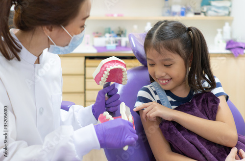 asian woman dentist with smiling face teaching young child how to brush teeth and take care of tooth health with dental model in clinic of hospital. healthcare and medical concept