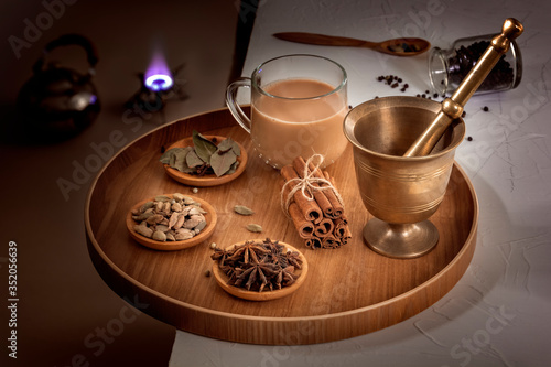 Masala tea in a glass cup and a natural mixture for its preparation - star anise, cinnamon sticks, cardamom, bay leaf, pepper and pepper on a wooden dish. Low key