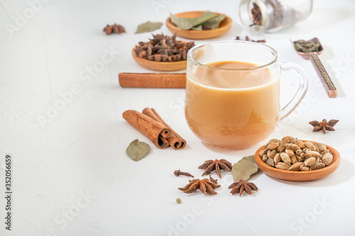 Masala tea in a glass cup and a natural mixture for its preparation - star anise, cinnamon sticks, cardamom, bay leaf, pepper and pepper on a white wooden table. Copy space