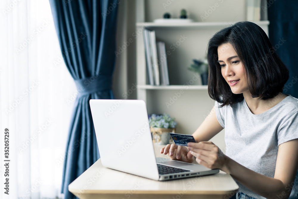 Young beautiful Asian woman holding credit card shopping online from home. Girl using laptop computer for buy items from internet during Covid19 pandemic at house. New normal modern purchase concept. Young beautiful Asian woman holding credit card shopping online from home. Girl using laptop computer for buy items from internet during Covid19 pandemic at house. New normal modern purchase concept.