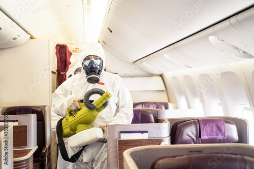 Cleaner officers hold cleaning device on airplane passenger cabin. An employee sprays disinfectant aboard a plane, during airline's sanitary measures to help curb the spread of Coronavirus pandemic. photo