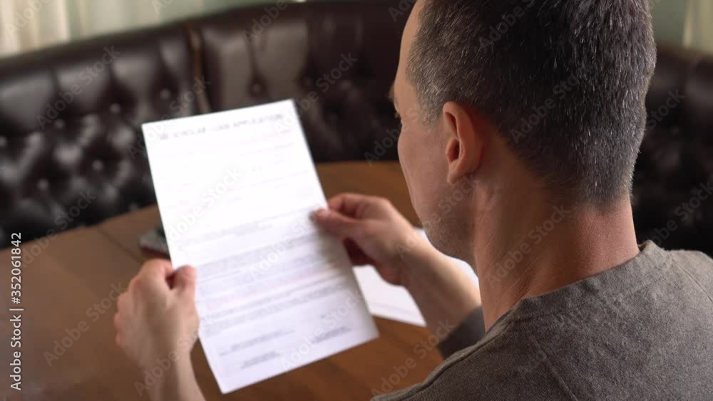 Financial Crisis and Bank Lending. Sad adult man reads a loan application and doubts, thinks and signs it. Family financial problems Financial Crisis and Bank Lending. Sad adult man reads a loan application and doubts, thinks and signs it. Family financial problems