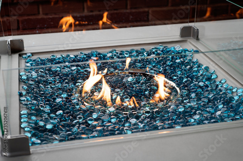 Modern lit gas fire pit with blue glass marbles in an outdoor setting