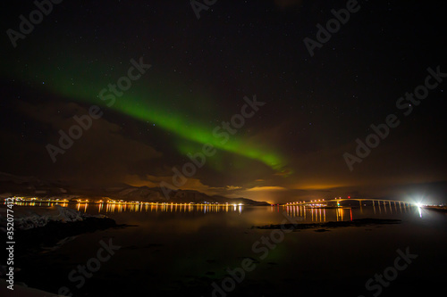 Green northern lights are soaring over a bridge near Stokmarknes in northern Norway. The green color is caused by electrons from space collide with oxygen molecules in the atmosphere. photo