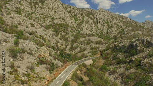 Aerial shot of car on highway over rocky mountain against sky, drone ascending over road on sunny day - Pag, Croatia photo