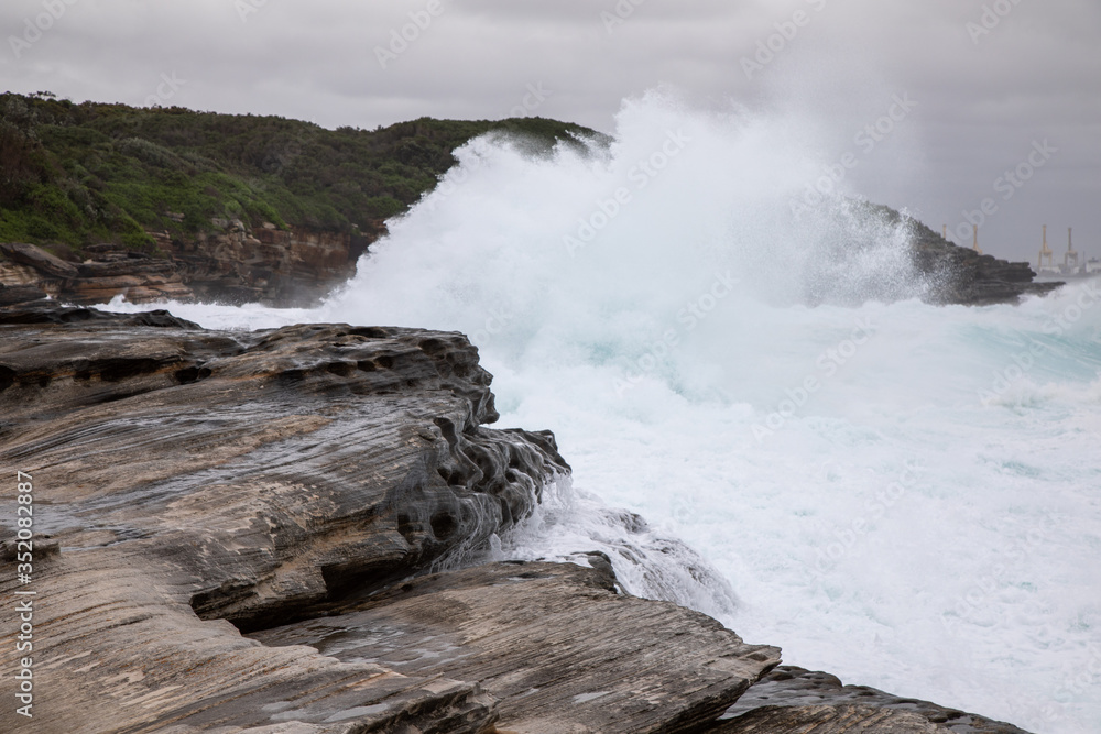 Storm in the ocean. Cloudy sky. Big waves are crashing into the rocks making white foam.