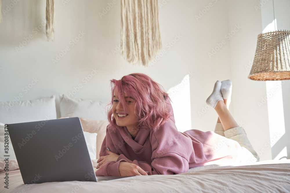 Happy hipster gen z teen girl with pink hair wear hoodie watching tv movie  on laptop