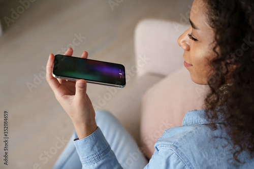 Canvas Print Young african woman user holding mobile phone in hand speak on speakerphone using virtual digital voice recognition assistant search on smartphone record audio message, mobile app ai tech assistance