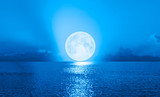 Full moon rising over empty ocean at night with power wave 