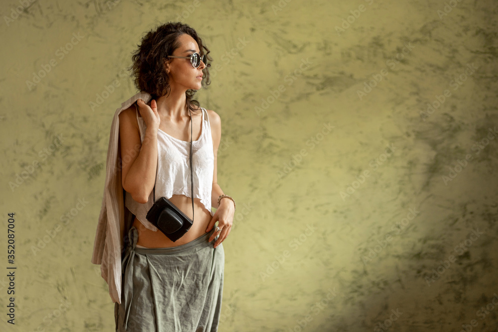 Obraz premium A girl with sunglasses and a camera against the wall. The concept of travel. Copy space