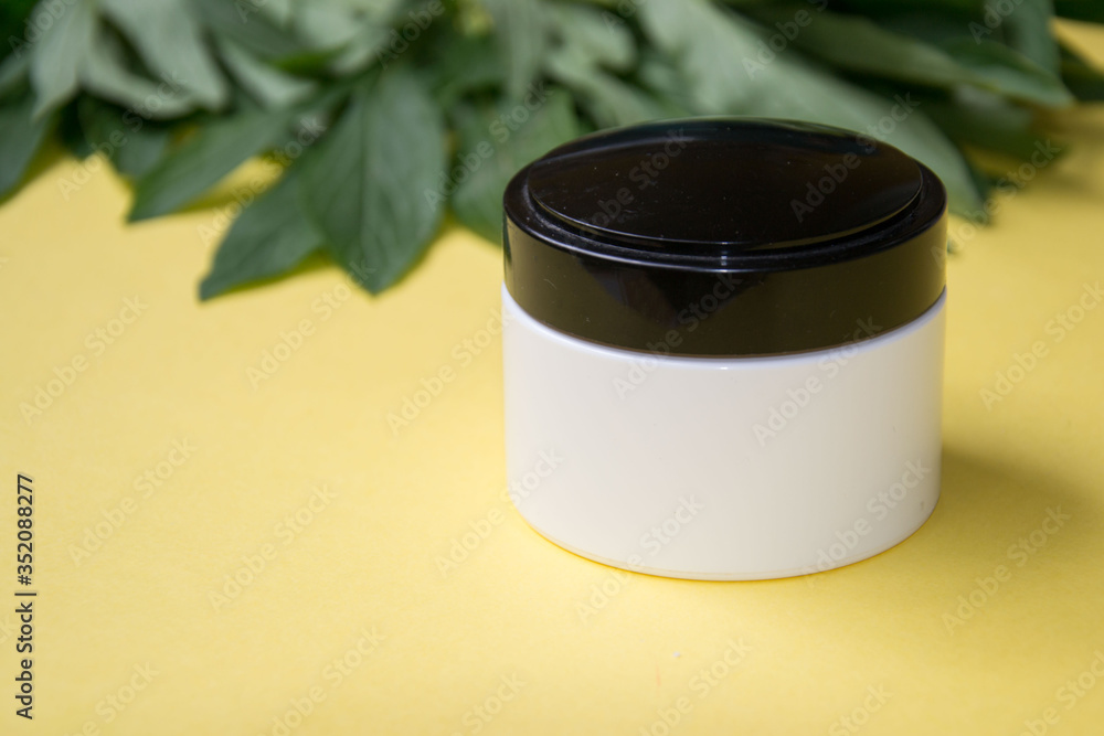 Jar with cosmetic cream, facial skin care, green peony leaves on yellow background, copy space, packaging mockup, product design Jar with cosmetic cream, facial skin care, green peony leaves on yellow background, copy space, packaging mockup, product design