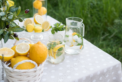 Lemonade with lemon, mint and ice on garden table. Preparation of the lemonade drink. Lemonade in the jug and lemons with mint on the table outdoor.