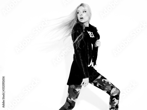 Young beautiful hipster girl in black leather jacket and stylish fashionable tight military pants leggings.Model with earring in nose.Sexy woman walking and jumping in studio.Flying hair in motion