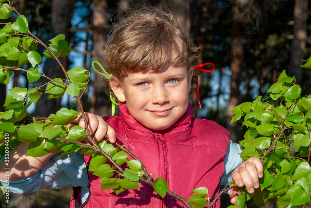 A beautiful girl with blue eyes stands near birch branches. Photo on a forest background. A beautiful girl with blue eyes stands near birch branches. Photo on a forest background.