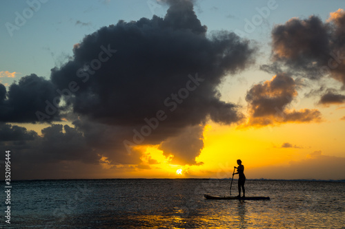 Girl surfer coming back from the ocean by paddle board against the backdrop of a beautiful sunset in Mauritius