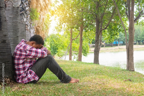 Asia you man sitting alone.He sitting in park under big tree.man very sad and depressed.sad,alone,suicide.despair. sickness.photo health and disappointment concept.