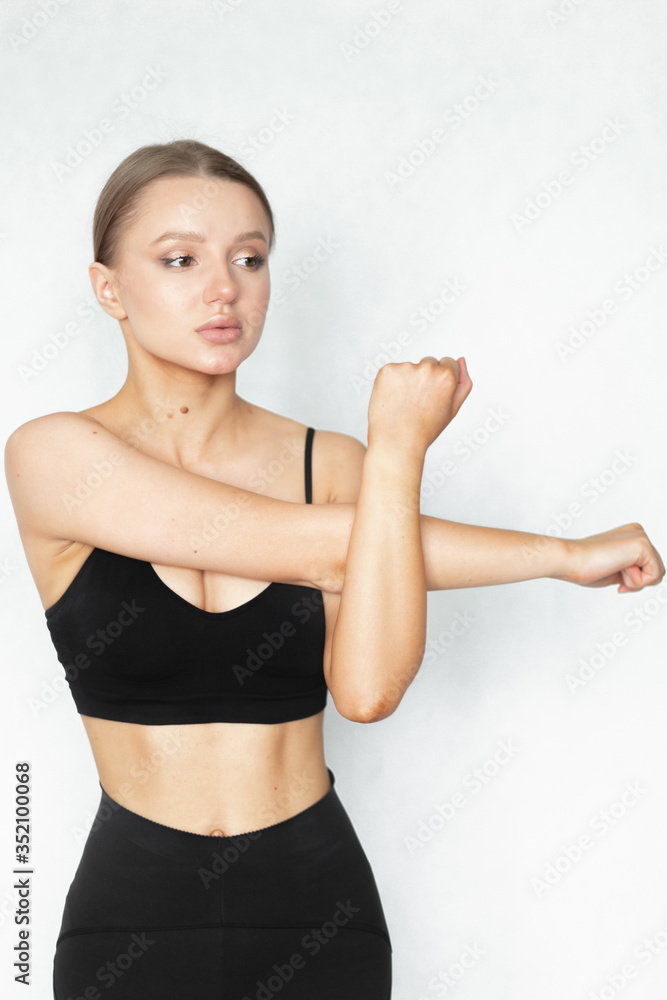 Beautiful caucasian woman with a perfect figure flexes her arm muscles on a white background. Sportswear. Warm up before weight loss training. Beautiful caucasian woman with a perfect figure flexes her arm muscles on a white background. Sportswear. Warm up before weight loss training.
