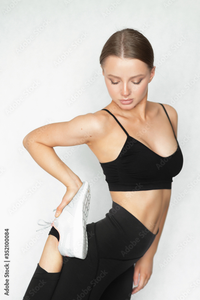 Beautiful caucasian woman with a perfect figure stretches leg muscles on a white background. Sportswear. Healthy lifestyle and weight loss. Beautiful caucasian woman with a perfect figure stretches leg muscles on a white background. Sportswear. Healthy lifestyle and weight loss.