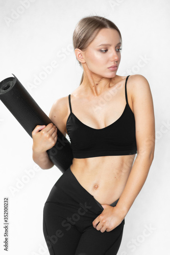A caucasian woman with a great figure in sportswear and a yoga mat poses on a white background and shows perfect abdominal muscles. Mat For Fitness. Personal care and sports at home.