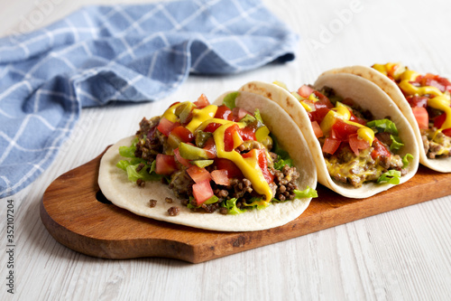 Homemade Cheeseburger Tacos on a rustic wooden board on a white wooden table, side view. Close-up.