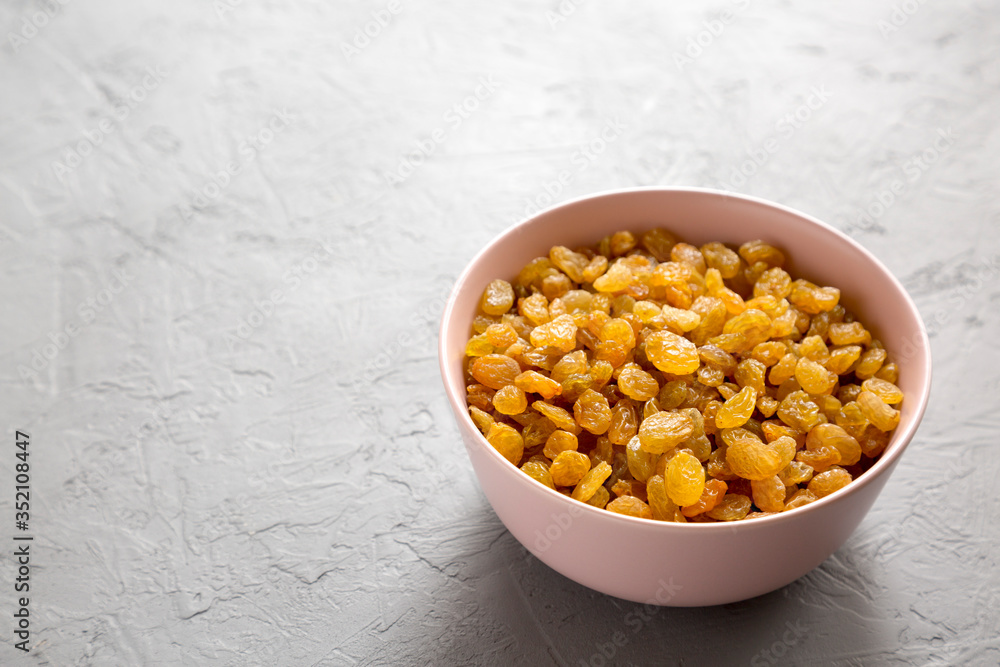 Golden Raisins in a Pink Bowl on a gray background, side view. Copy space. Golden Raisins in a Pink Bowl on a gray background, side view. Copy space.