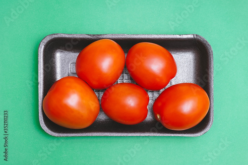 Tomatoes in a black plastic container on a green background. Top view. Shiny vegetables.