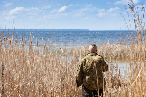 A man looks at a large river from the reeds, view from the back.