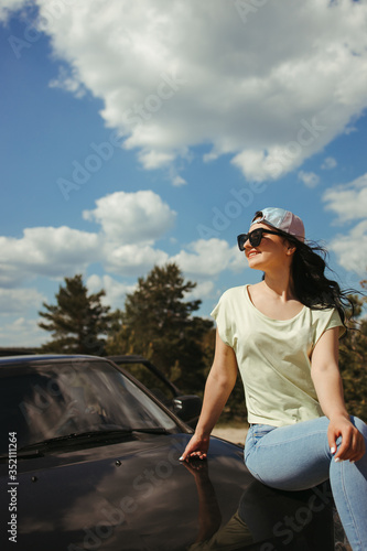 Young woman sitting on the car hood while traveling. Tourism lifestyle, vacation, freedom and travel concept © Vadym