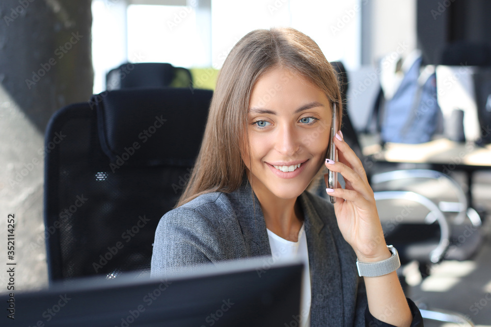 Beautiful business woman is talking on the mobile phone and smiling while sitting in modern office. Beautiful business woman is talking on the mobile phone and smiling while sitting in modern office.