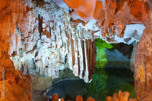 A lake, stalactite and stalagmite formations and vandalizing signs in Russian in a limestone cave of Halong Bay, Vietnam
