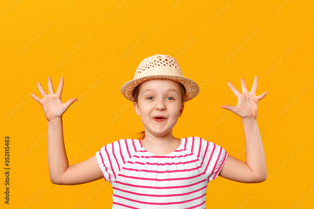Cheerful happy cute little girl in a straw hat laughs and shows palms. Closeup portrait of a child on a yellow background Cheerful happy cute little girl in a straw hat laughs and shows palms. Closeup portrait of a child on a yellow background